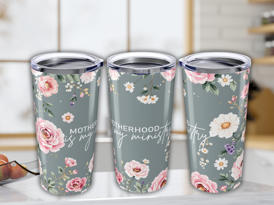 Three floral travel mugs on a kitchen counter. Each features pink and white flowers against a gray background with the text, "Motherhood is my ministry."