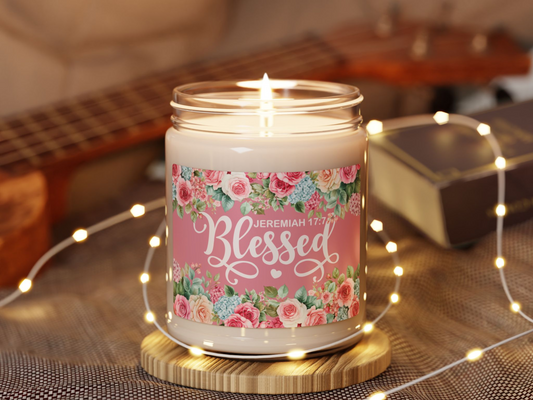 A lit candle with a floral "Blessed" label sits on a wooden coaster, surrounded by soft fairy lights. A guitar and book add a cozy, warm ambiance.