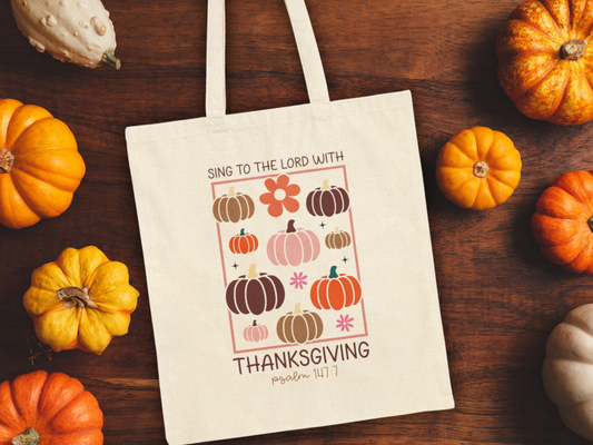 Tote bag on wooden surface surrounded by pumpkins for a festive fall display.