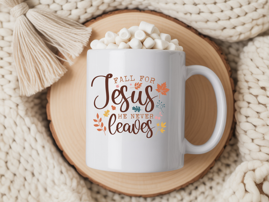 White mug with 'Fall for Jesus he never leaves' text, filled with hot chocolate and marshmallows, on a wooden coaster.
