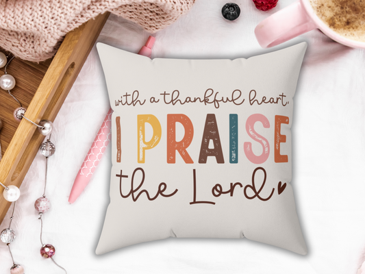 A decorative pillow features the phrase "With a thankful heart, I praise the Lord" in colorful, bold text. Cozy elements surround the pillow: a pink pen, knitted fabric, pearls, berries, and a cappuccino, creating a warm, inviting ambiance.
