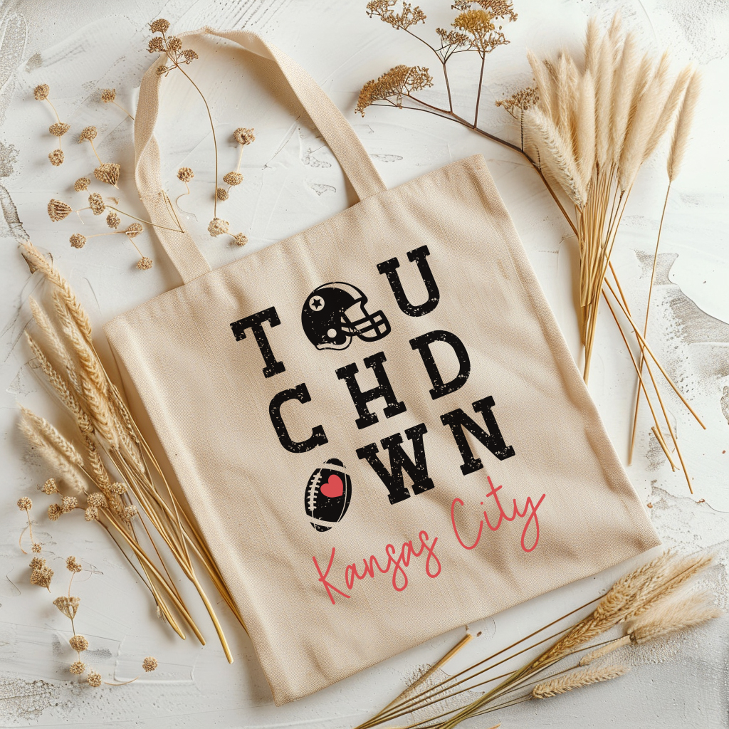Beige tote bag with 'Touchdown Kansas City' text on a light background with dried plants.