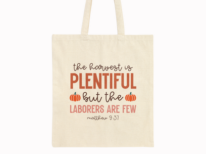 Beige tote bag with quote: "The harvest is plentiful but the laborers are few. Matthew 9:37." Features decorative pumpkins, autumn tones.
