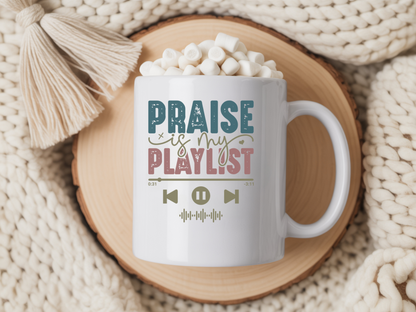 White mug with 'Praise is my playlist' text on a wooden coaster with hot chocolate and marshmallows.