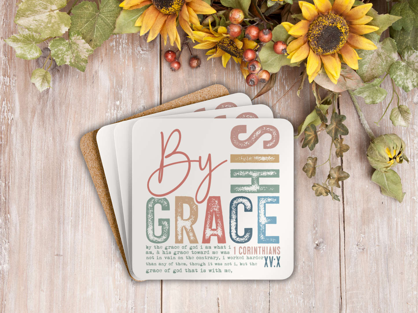 Stack of Bible verse coasters with cork backing styled on rustic wooden surface with sunflowers and greenery.