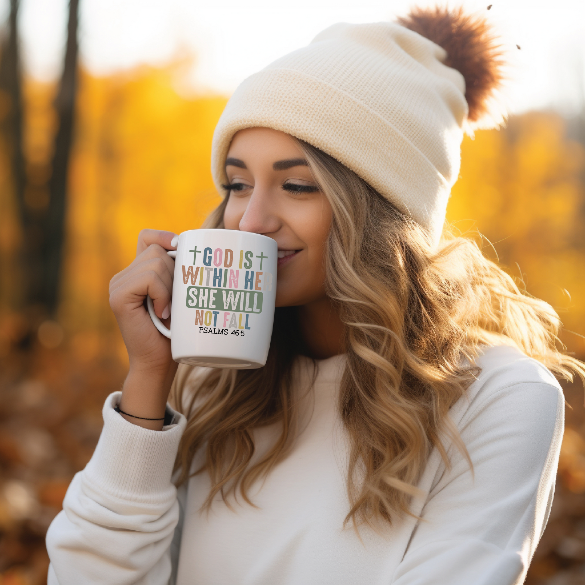 Woman in a white beanie and sweater holding a mug with a motivational quote in an autumn setting.
