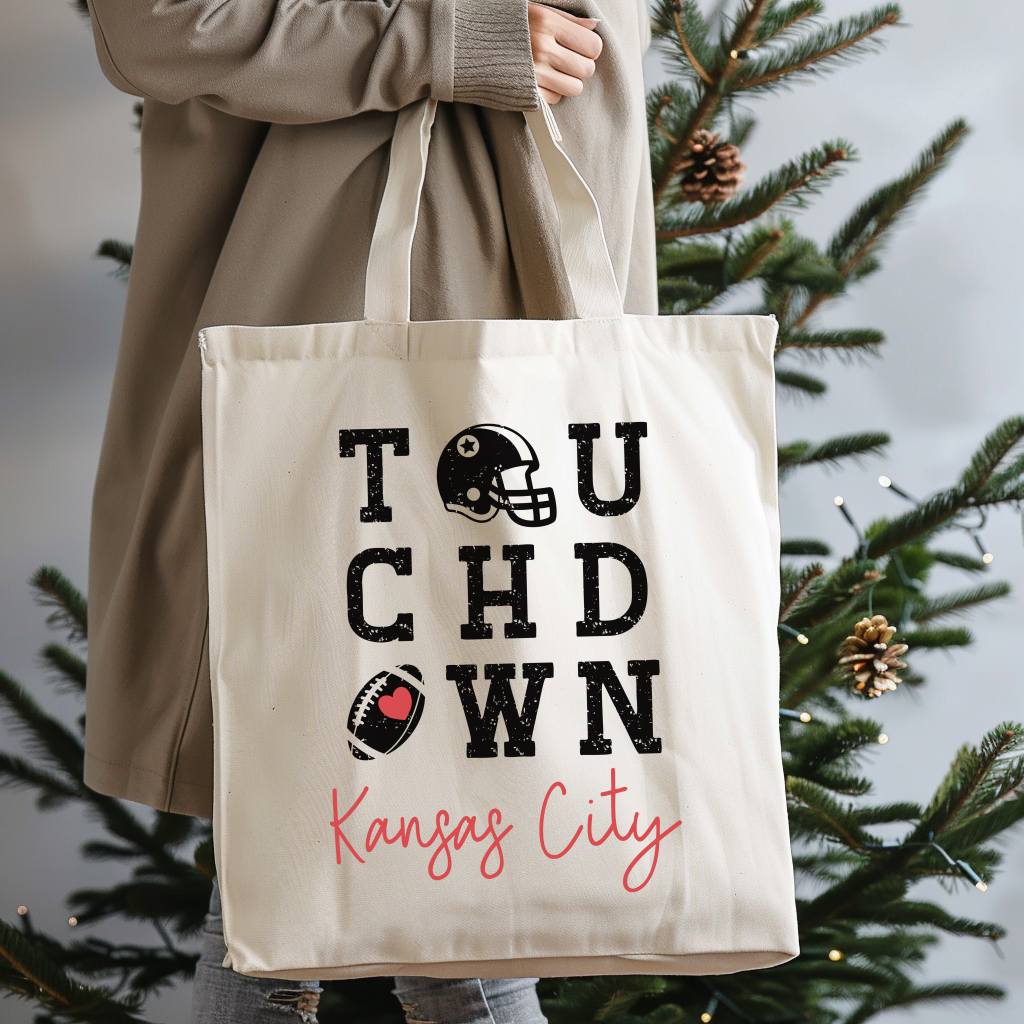 Tote bag with 'Touchdown Kansas City' text held by a person in front of a Christmas tree.