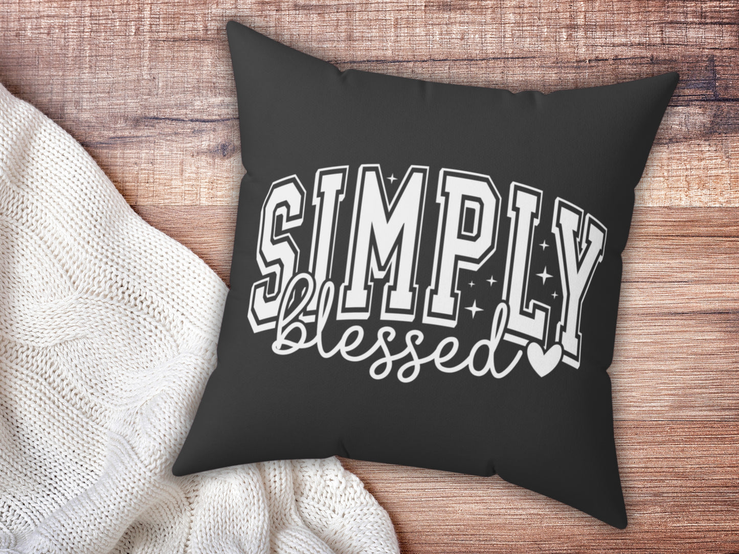 Black pillow with 'Simply Blessed' text on a wooden surface