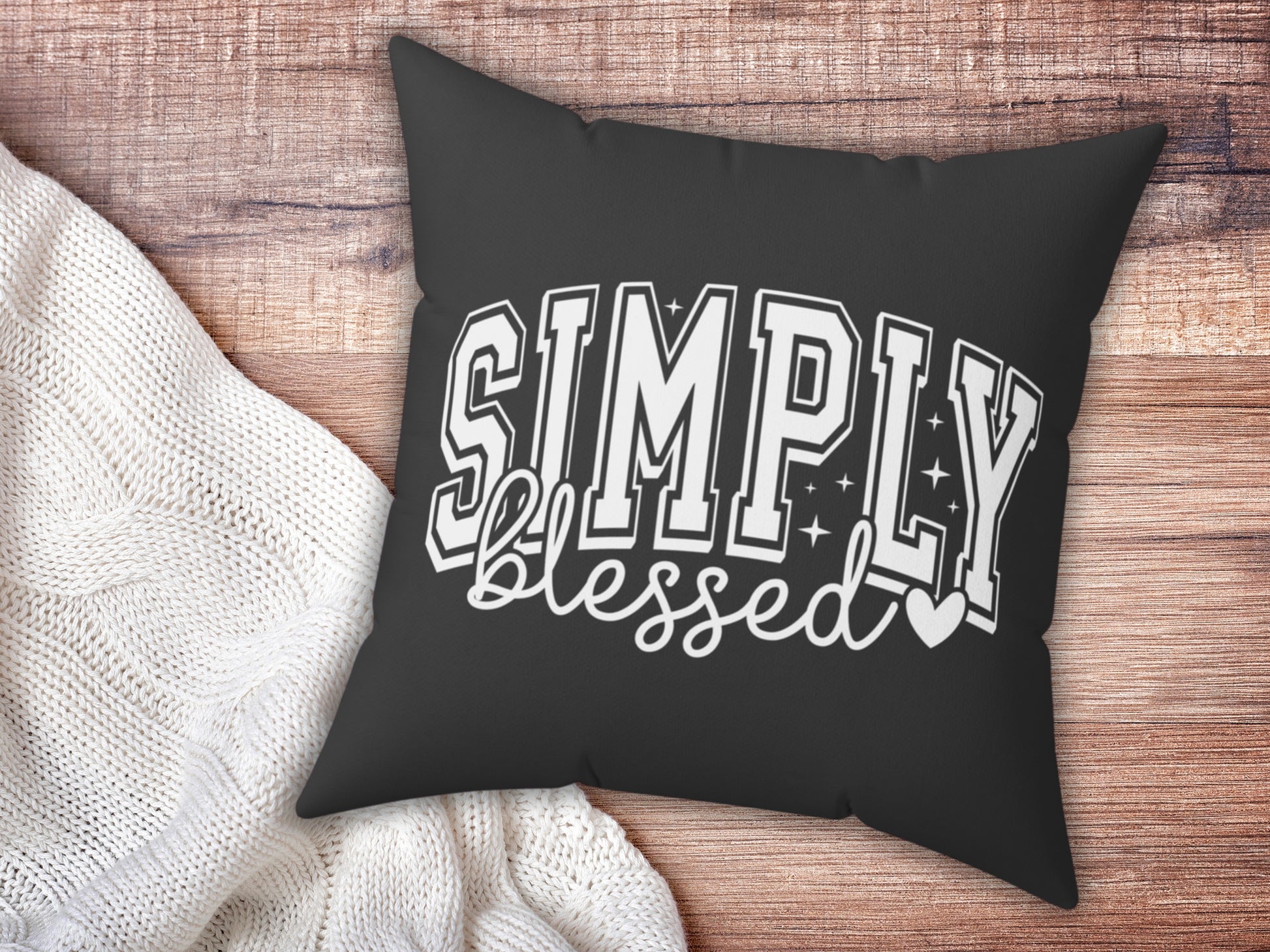 Black pillow with 'Simply Blessed' text on a wooden surface