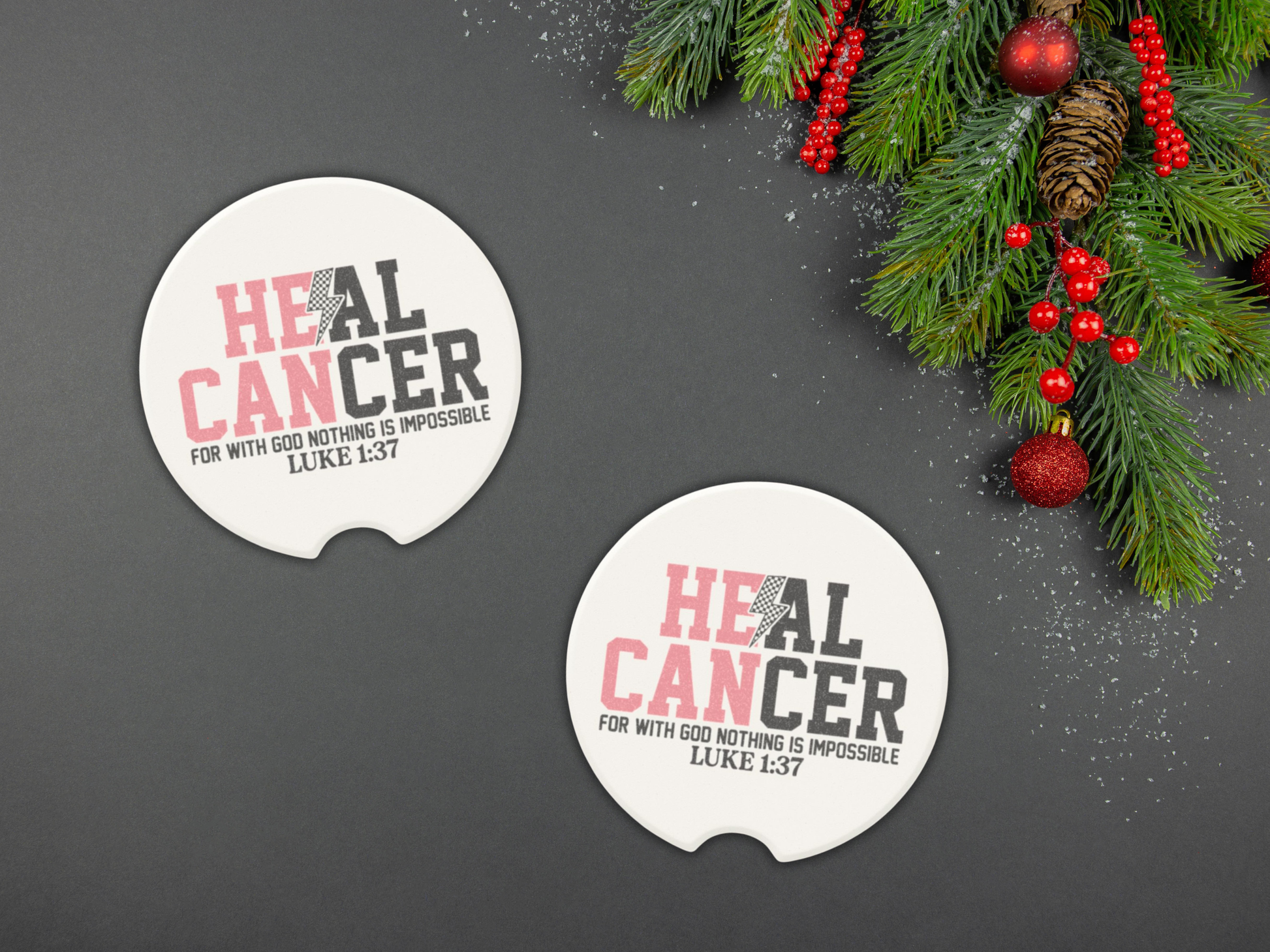 Two 'HEAL CANCER' coasters on a dark surface with Christmas decorations.