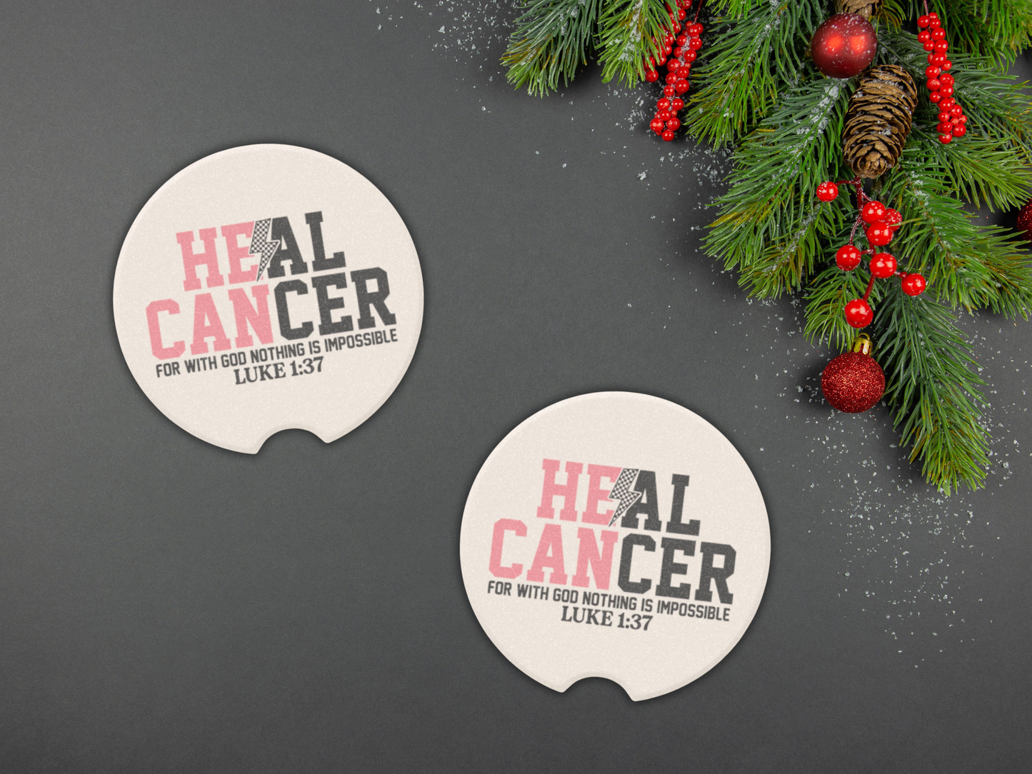 Two 'HEAL CANCER' car coasters on a dark surface with Christmas decorations.