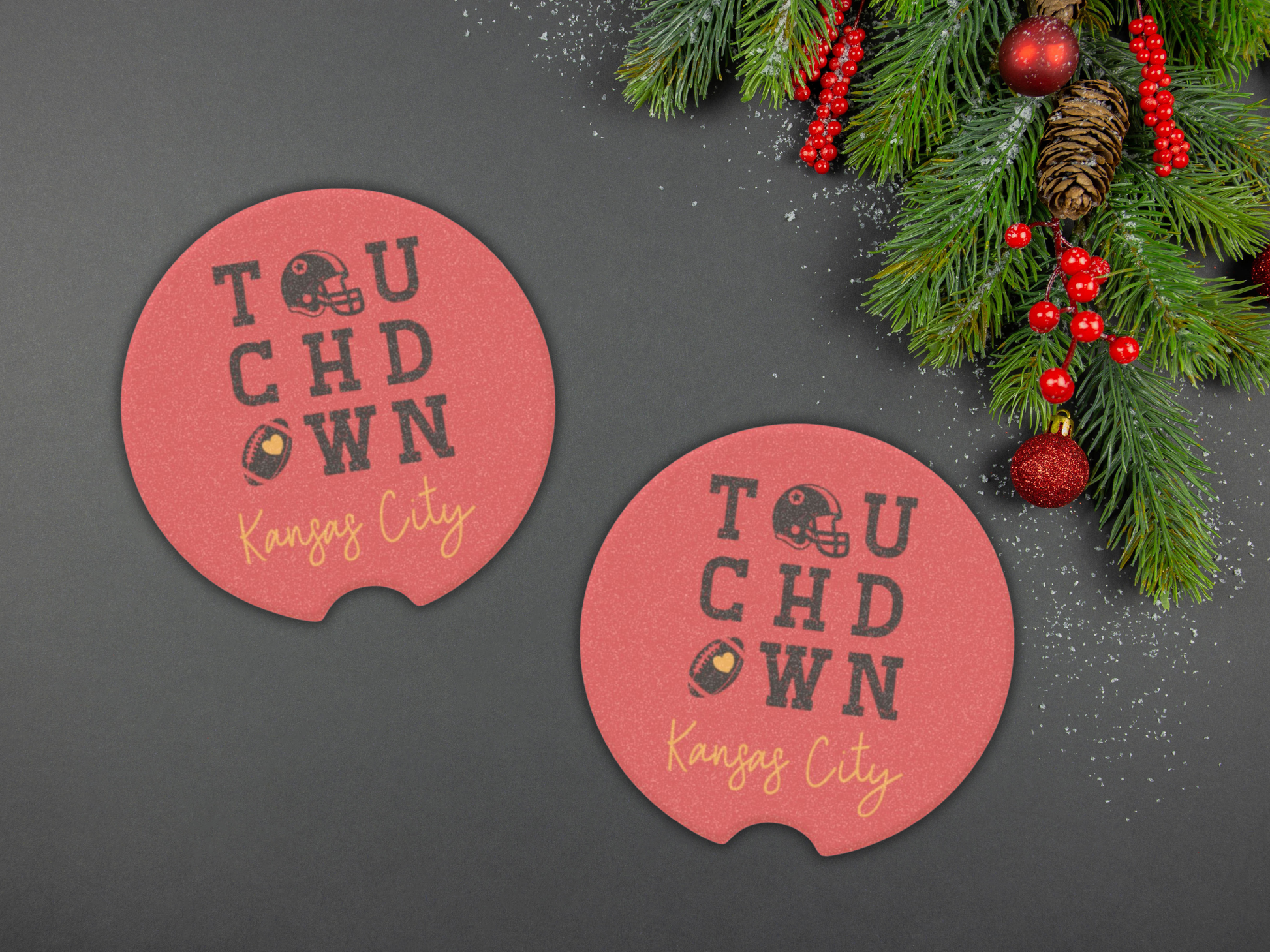 Two red coasters with 'Touchdown Kansas City' text on a dark surface with Christmas decorations.