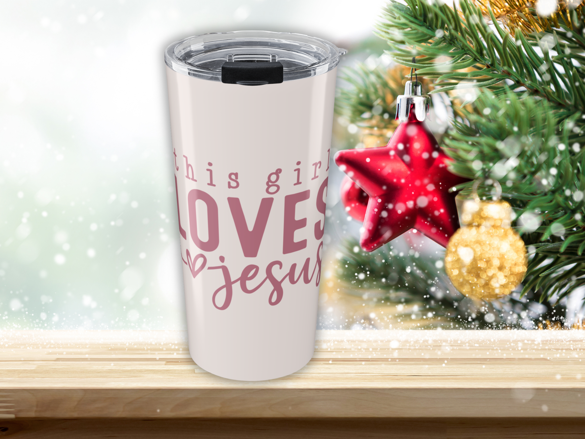 Tumbler with 'This girl loves Jesus' text in front of a Christmas tree with ornaments.