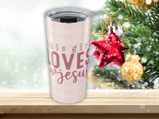 Tumbler with 'This girl loves Jesus' text next to Christmas decorations on a shelf.