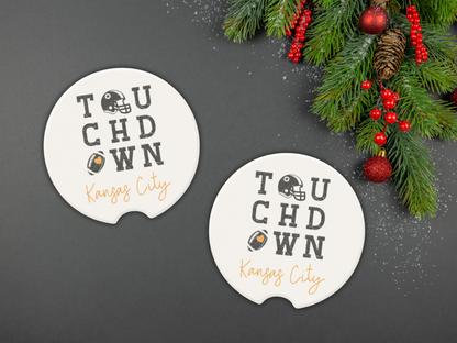 Two 'Touchdown Kansas City' coasters on a dark surface with Christmas decorations.