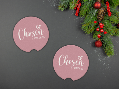 Two pink coasters with 'Chosen 1 Peter 1:2' text on a dark surface with Christmas decorations.