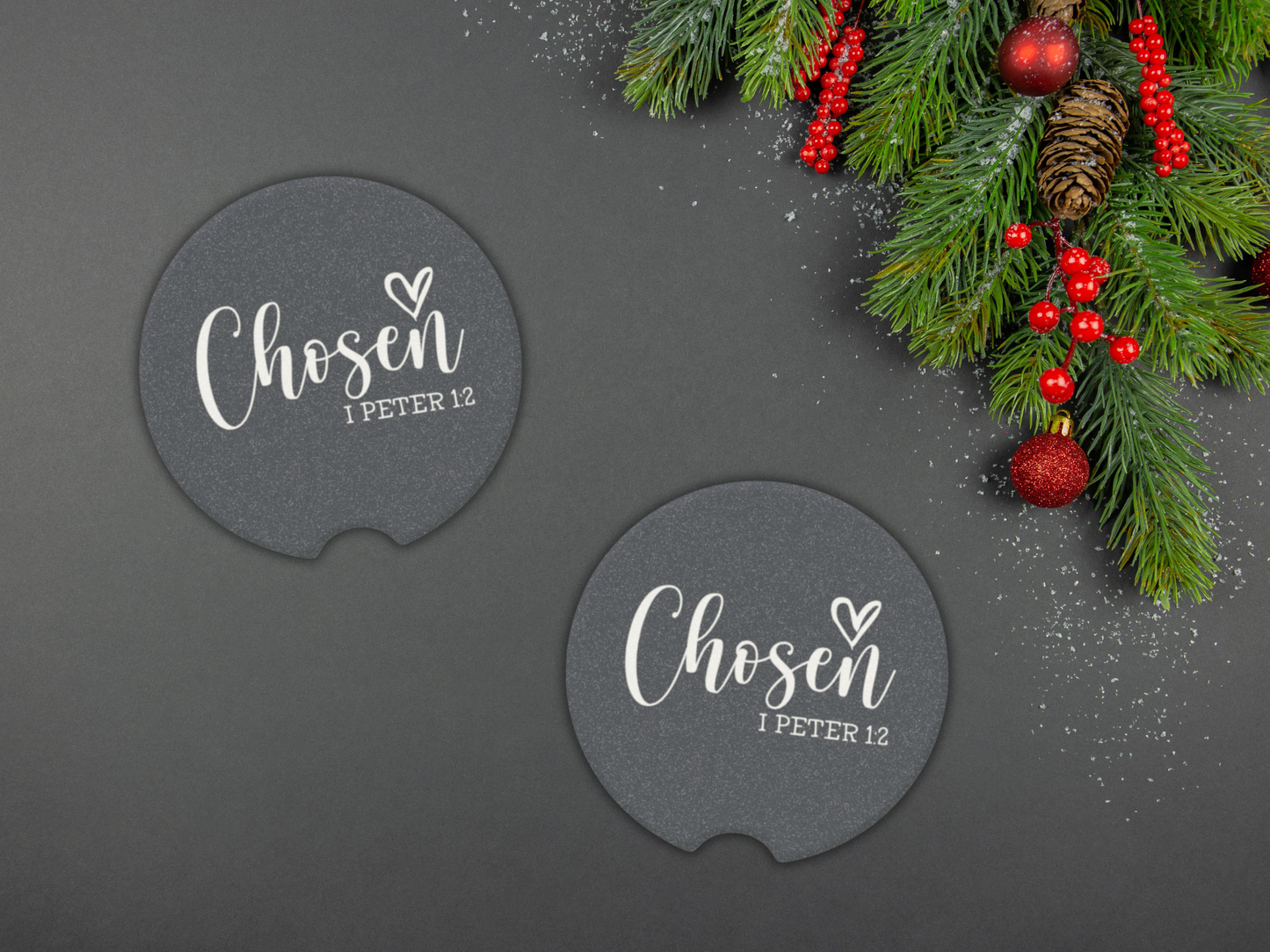 Two navy car coasters with 'Chosen I Peter 1:2' text on a dark surface with Christmas decorations.