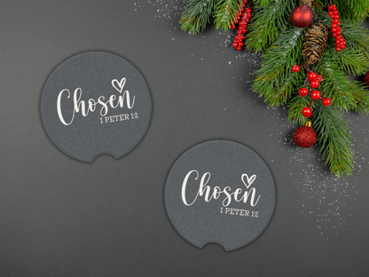 Two navy car coasters with 'Chosen I Peter 1:2' text on a dark surface with Christmas decorations.