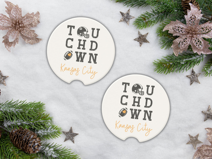 Two 'Touchdown Kansas City' coasters on a snowy surface with Christmas decorations.