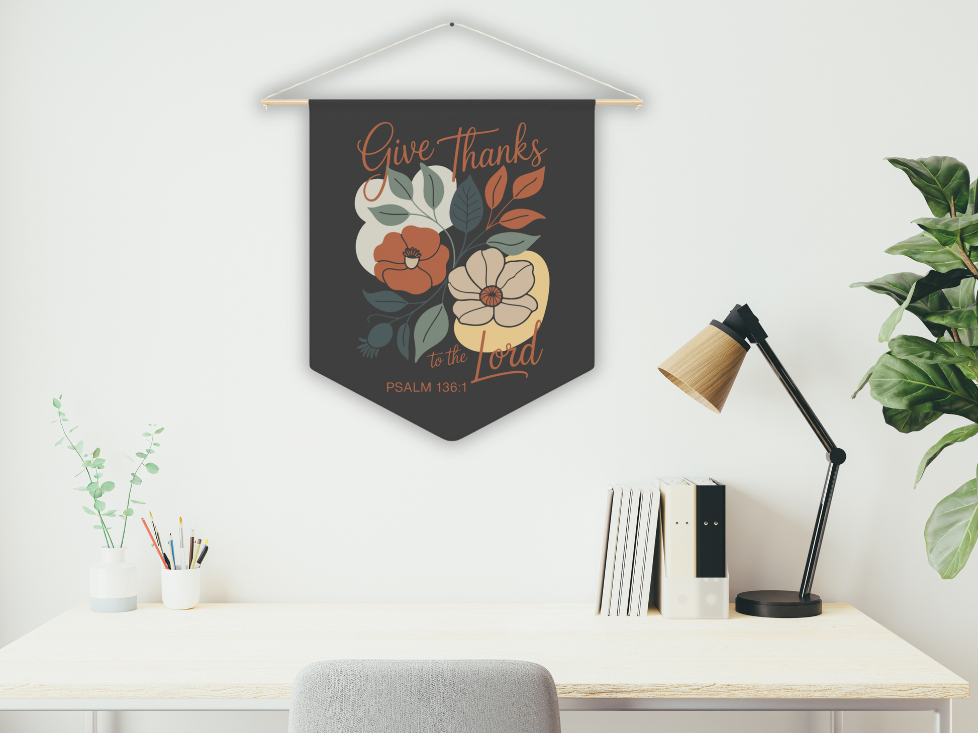 Decorative wall hanging with floral design and text above a desk with a lamp and books.