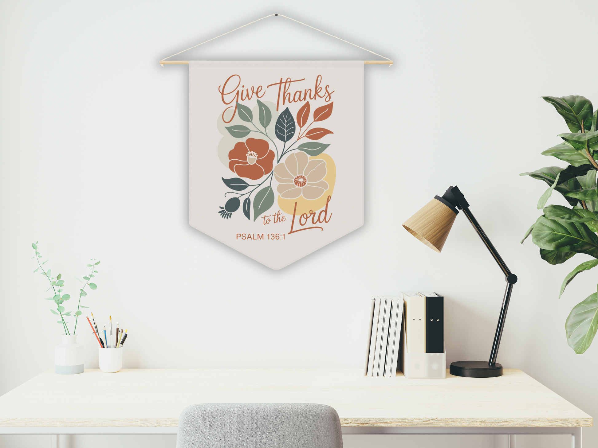 Decorative wall hanging with floral design and text above a desk with a lamp and books.