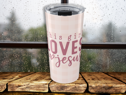 Pink tumbler with 'This girl loves Jesus' text on a wooden surface with a blurred outdoor background.