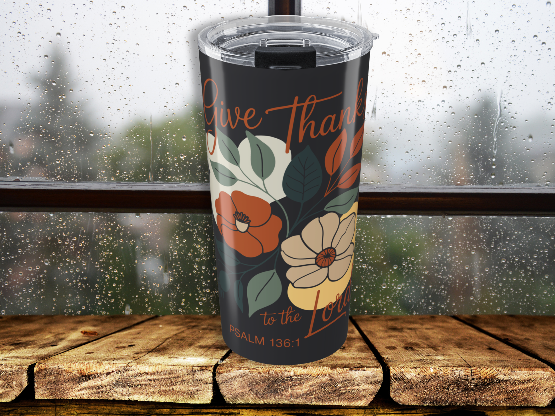 Tumbler with floral design and text on a wooden surface with a rainy window background