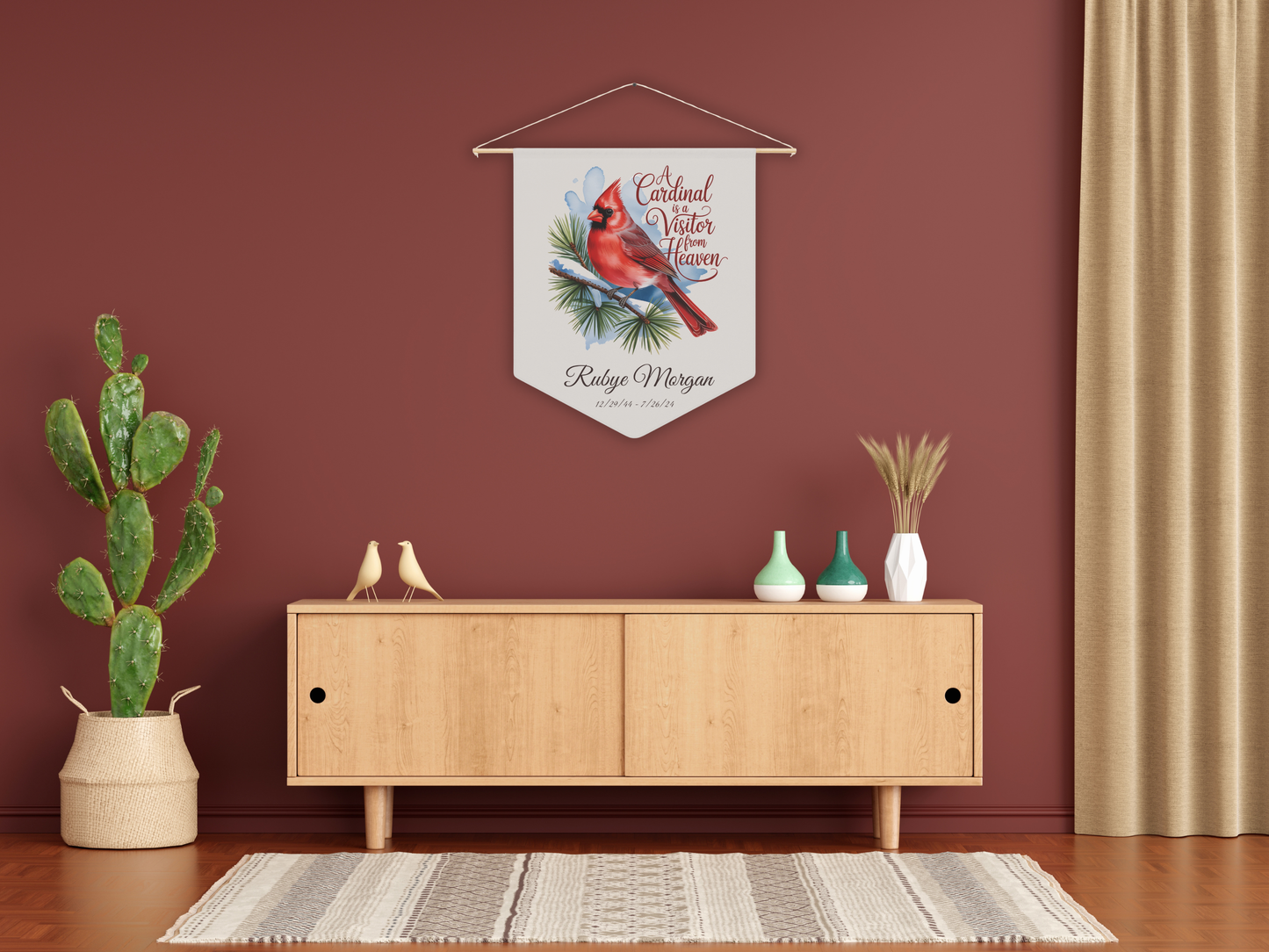 Decorative wall hanging with a cardinal design above a wooden cabinet in a room with a red wall.