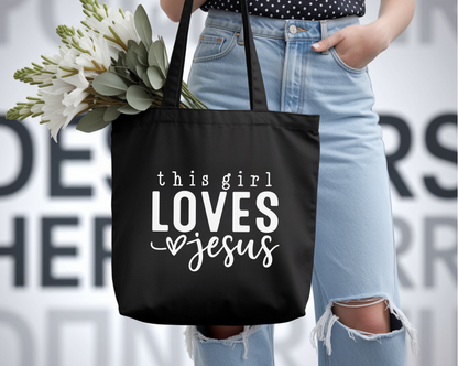Person holding a black tote bag with 'this girl LOVES jesus' text, wearing light blue jeans.