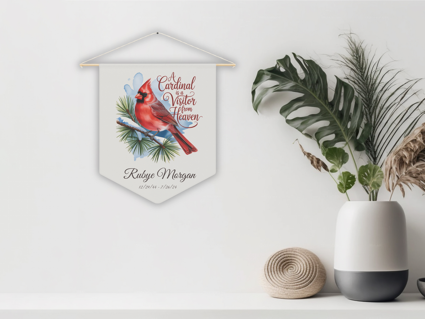 Decorative wall hanging with a cardinal illustration on a white wall with plants and a vase.