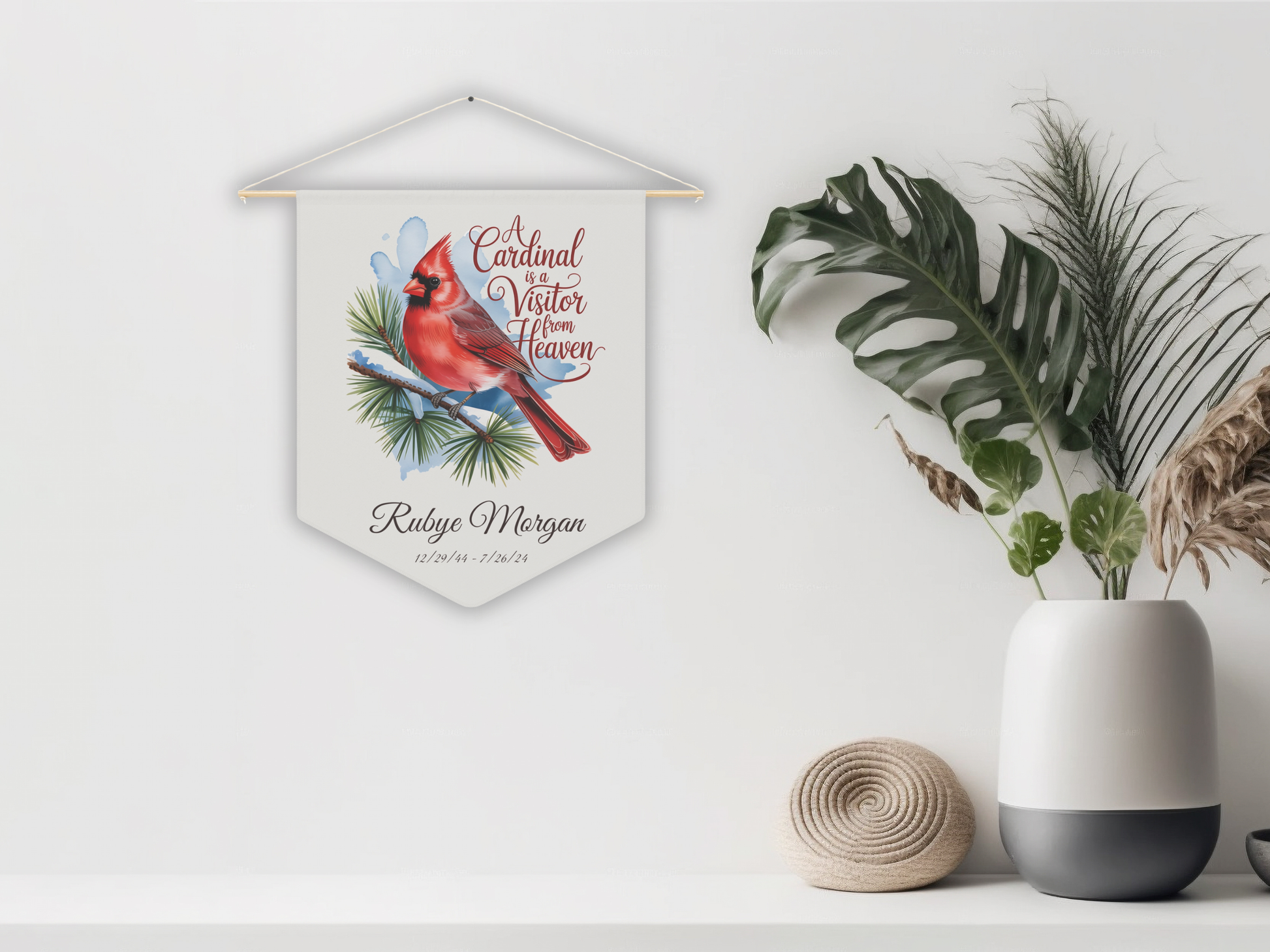 Decorative wall hanging with a cardinal illustration on a white wall with plants and a vase.