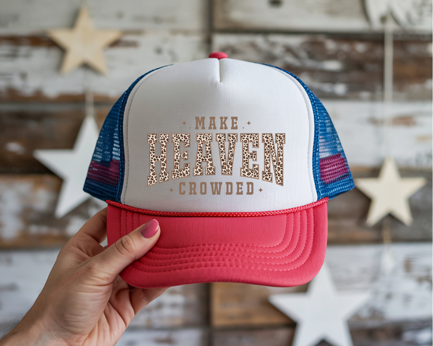 Trucker hat with 'Make Heaven Crowded' text held by a hand against a wooden wall with stars.