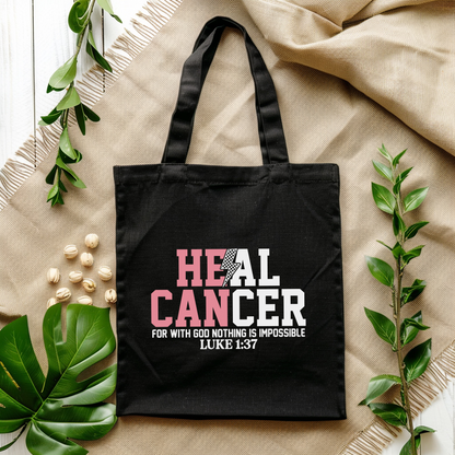 Black tote bag with motivational quote on a beige fabric background with green leaves.