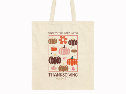 Beige cotton canvas tote bag with pumpkins, florals, and scripture “Sing to the Lord with Thanksgiving – Psalm 147:7” on plain background.