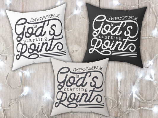 Three pillows with 'Impossible is God's Starting Point' text on a wooden surface with string lights.