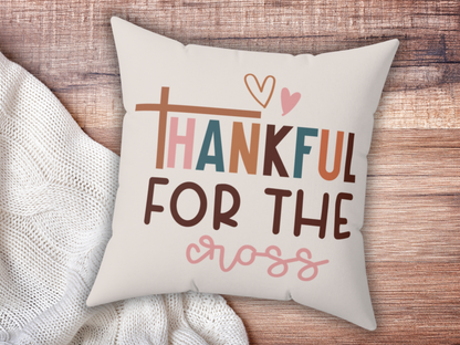 A decorative pillow on a wooden surface displays the text "Thankful for the Cross" in colorful, playful font with a heart design. Cozy and warm atmosphere.