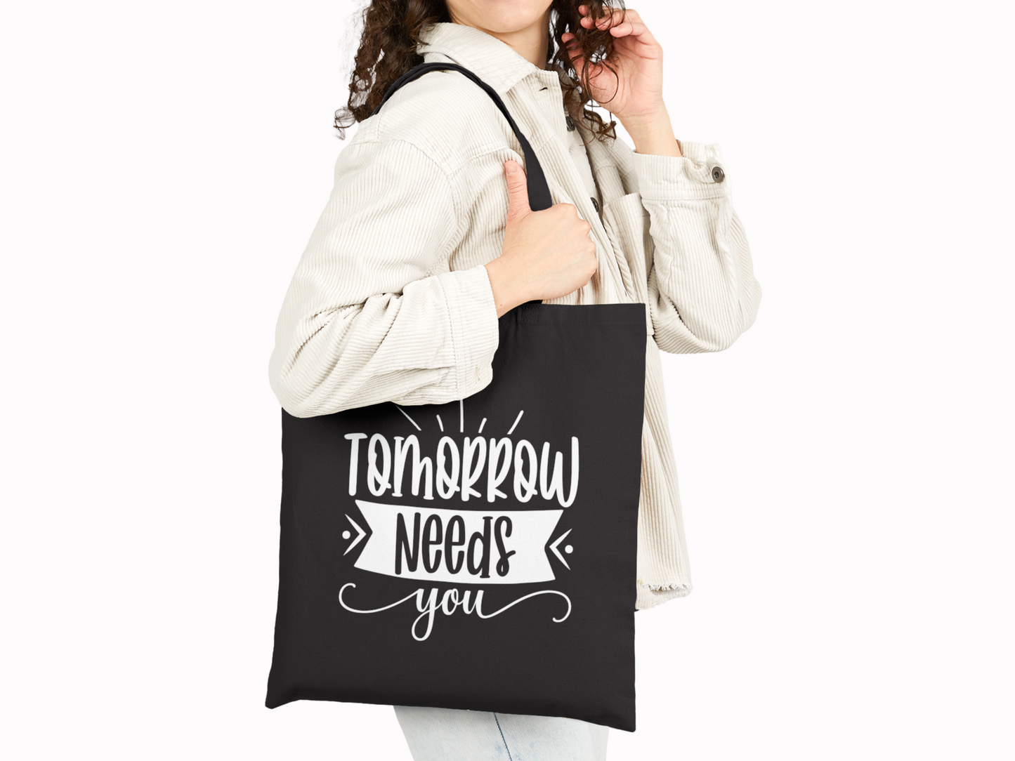 A person carries a black tote bag with bold, white lettering that reads, "Tomorrow needs you." They wear a light jacket, projecting an encouraging and hopeful tone.