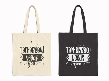 Two tote bags with motivational text "Tomorrow Needs You." The first bag is beige with black text, and the second is black with white text.