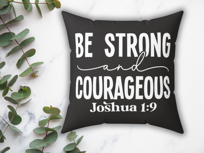 Black cushion with white text reading "Be Strong and Courageous Joshua 1:9" on a marble surface, surrounded by eucalyptus leaves, conveying encouragement.