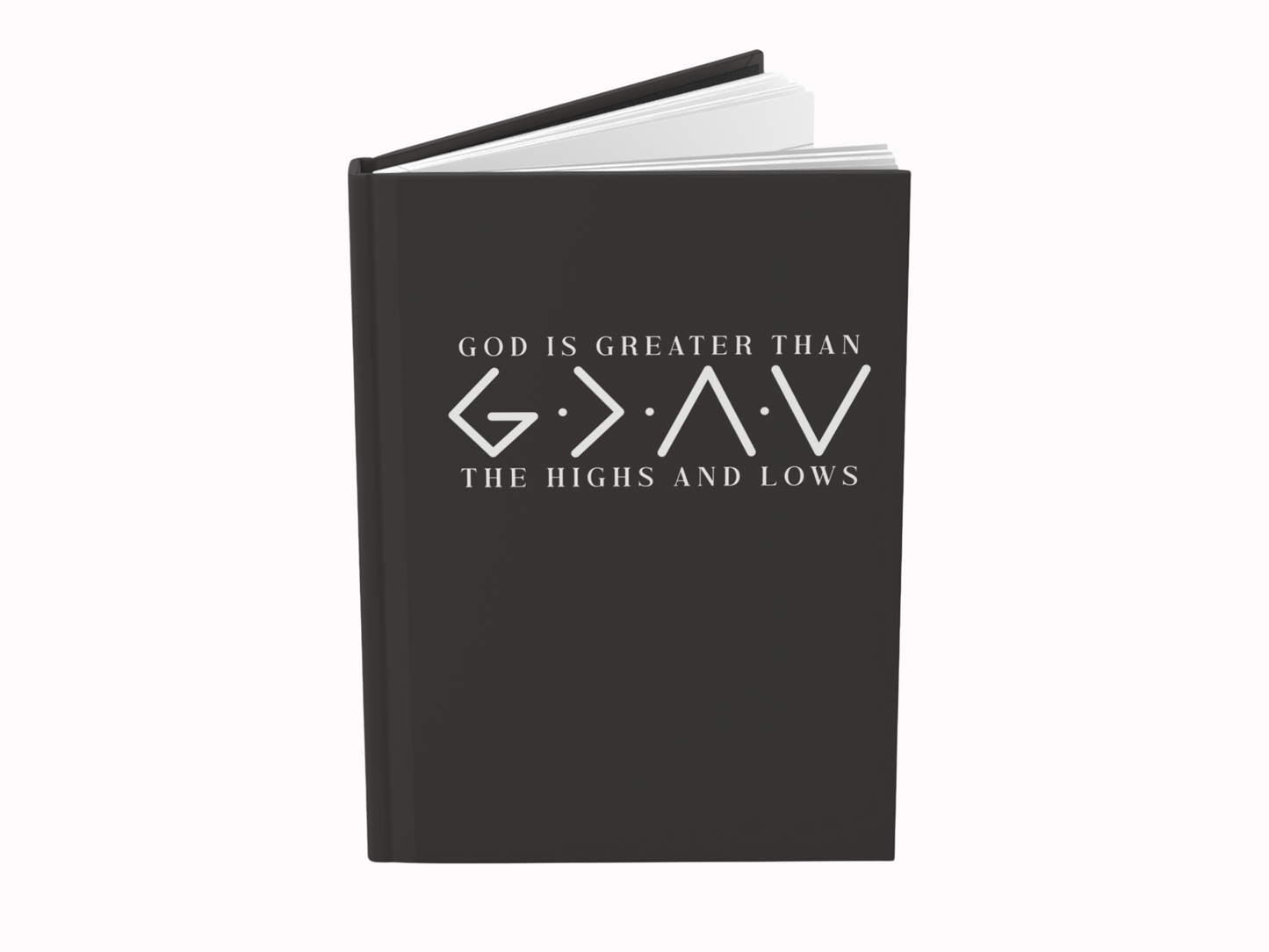 A black hardcover book is standing upright. The cover features the text "God is greater than the highs and lows" in white, conveying a spiritual theme.