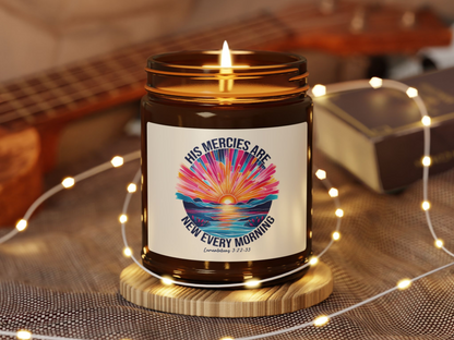 A lit candle with a label reading "His mercies are new every morning," showing a colorful sunrise. The setting is cozy with soft lights and a guitar.