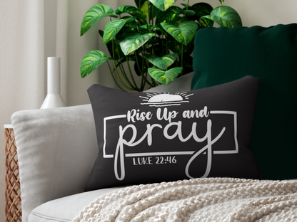 A black decorative pillow with white script reads "Rise Up and Pray, Luke 22:46" beside a cream blanket on a grey couch, with lush green plants nearby.