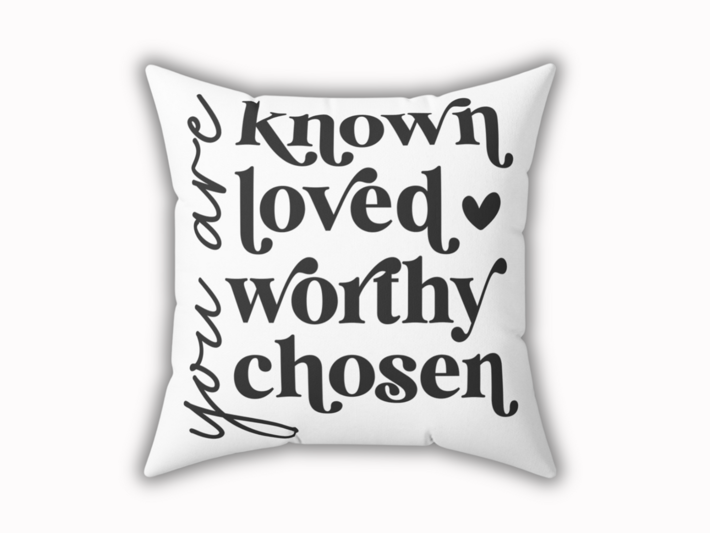 White square pillow with black text reading “you are known loved worthy chosen” in bold, elegant script. A small heart adds a warm touch.