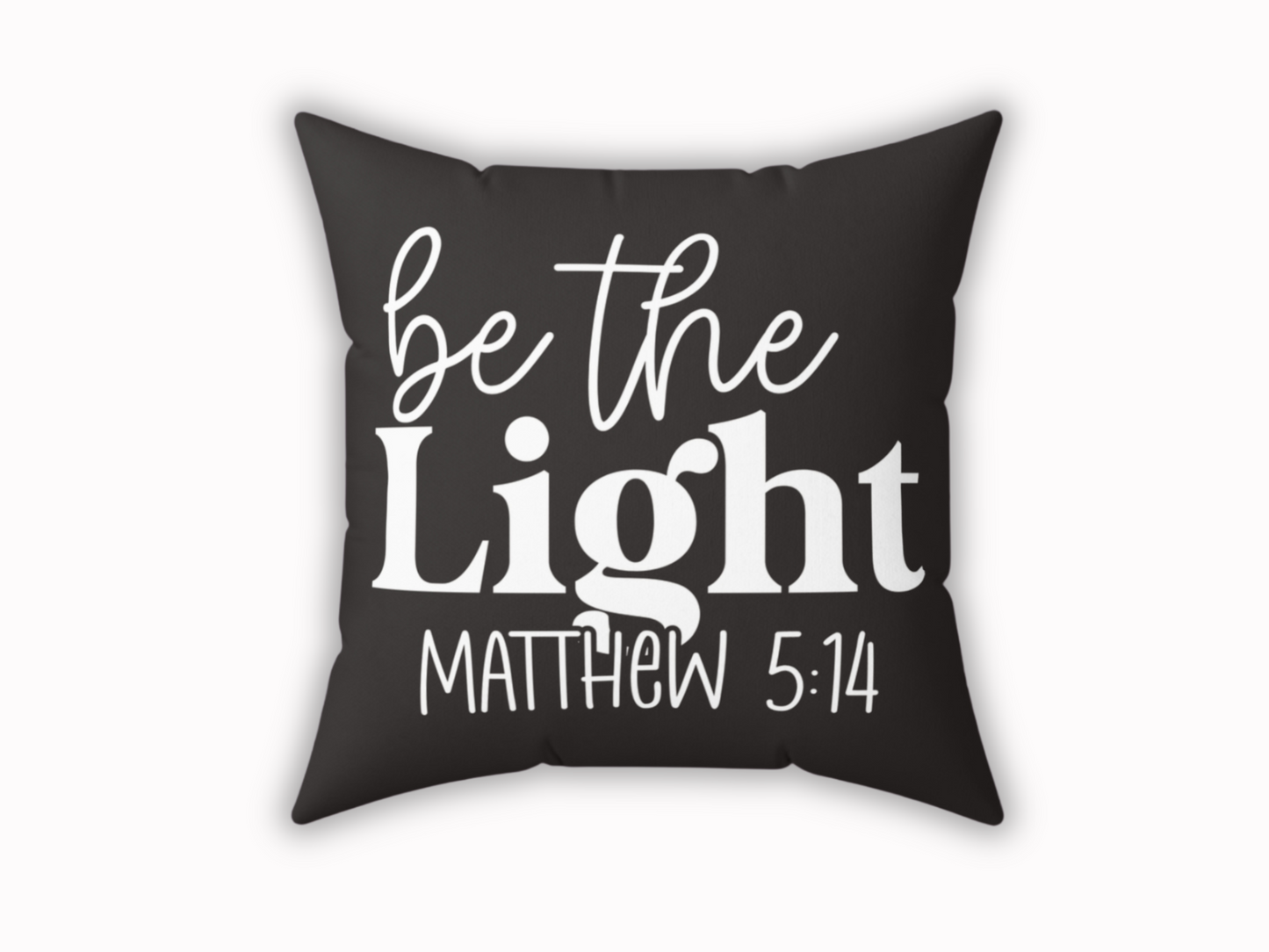 A black decorative pillow with the phrase "be the Light Matthew 5:14" in bold white letters. The design conveys a motivational and positive tone.