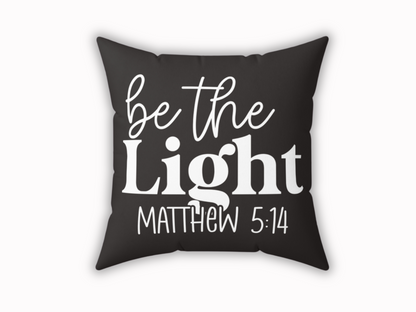 A black decorative pillow with the phrase "be the Light Matthew 5:14" in bold white letters. The design conveys a motivational and positive tone.