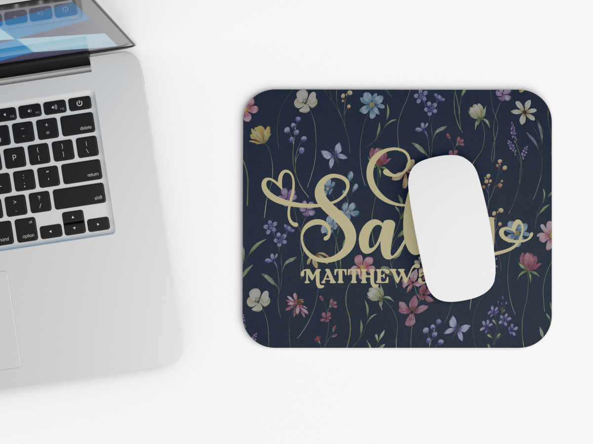 A laptop partially appears on the left, while a mousepad on the right features colorful wildflowers and elegant script text on a dark background, creating a harmonious work atmosphere.