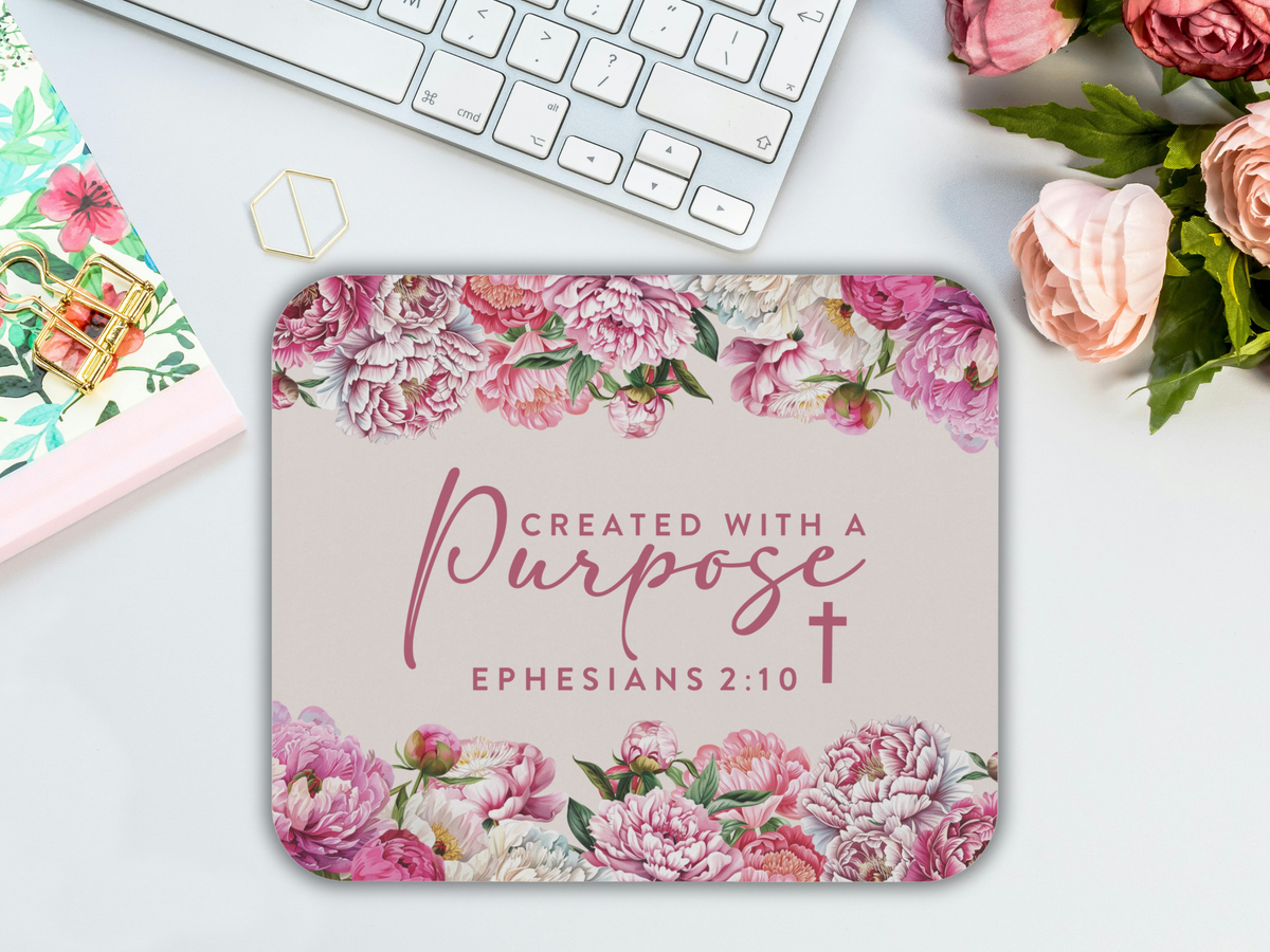 Floral mouse pad with the words "Created with a Purpose - Ephesians 2:10" in elegant script, surrounded by pink peonies, next to a keyboard.