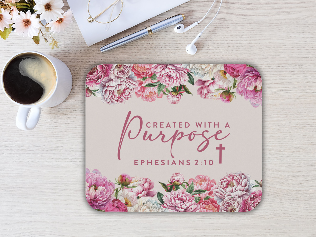 Mousepad with pink floral border and the text "Created with a purpose, Ephesians 2:10." Nearby a cup of coffee, glasses, pen, and earphones.