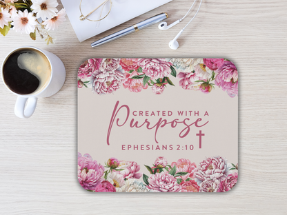 Mousepad with pink floral border and the text "Created with a purpose, Ephesians 2:10." Nearby a cup of coffee, glasses, pen, and earphones.