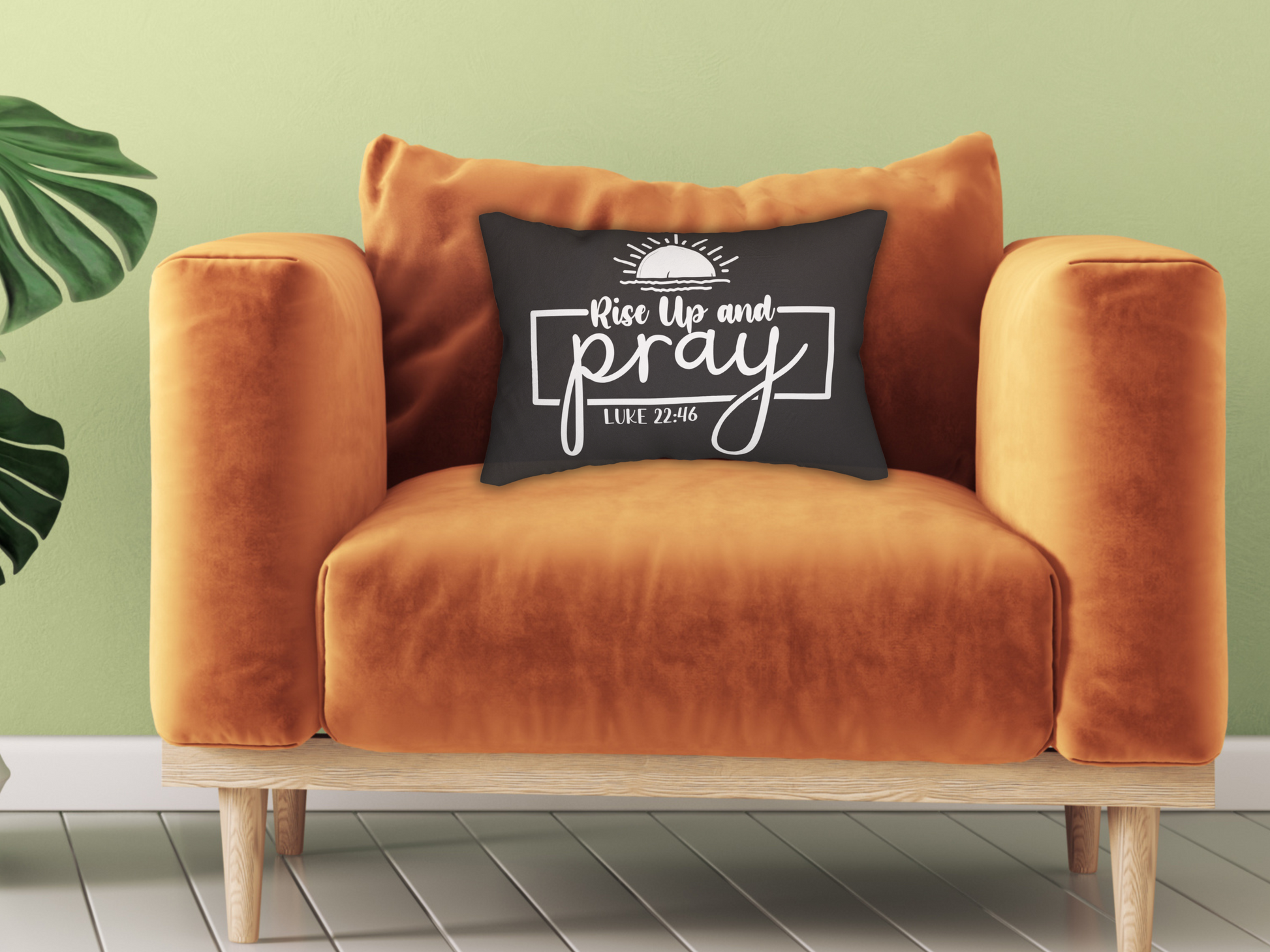 An orange velvet chair with a black cushion displaying "Rise Up and Pray, Luke 22:46" in white script. A green plant is in the background.